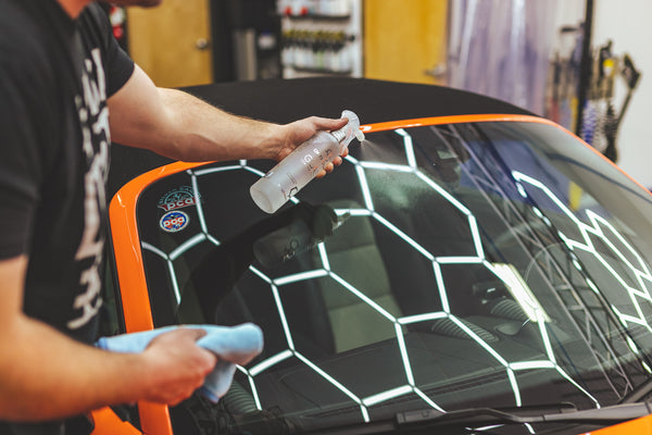 A closeup of a person spraying the front windshield of an orange Porsche with Opti-Coat Glass Cleaner.