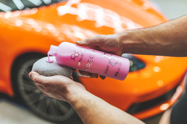 A person pouring Opti-Coat Tire Gel onto a grey circular applicator with a background of an orange car.