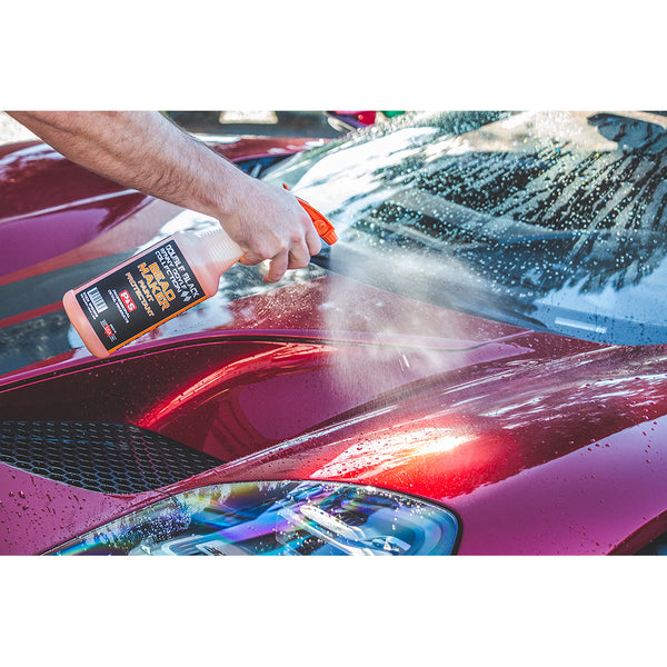 A person spraying bead maker on the front of a maroon car.