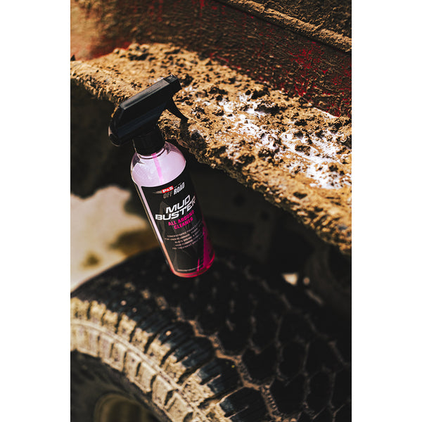 A spray bottle of P&S Mud Buster hanging off the tire well of a muddy jeep.