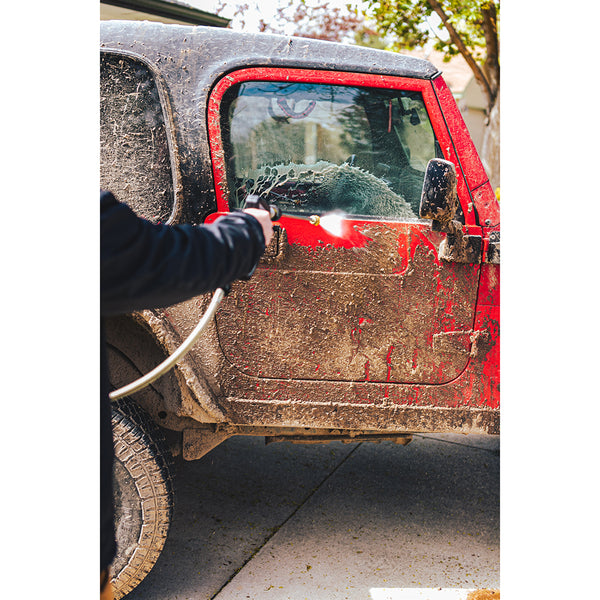 A person spraying off a red jeep covered in mud with a hose.