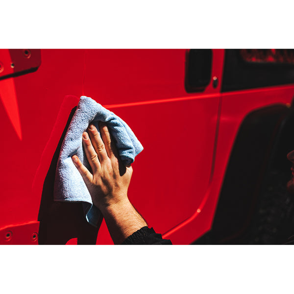 A closeup of a person wiping the door of a red jeep with a blue towel.