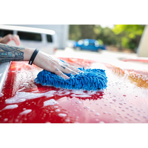 A closeup of a person scrubbing the roof of a red car with a blue chenille pad.