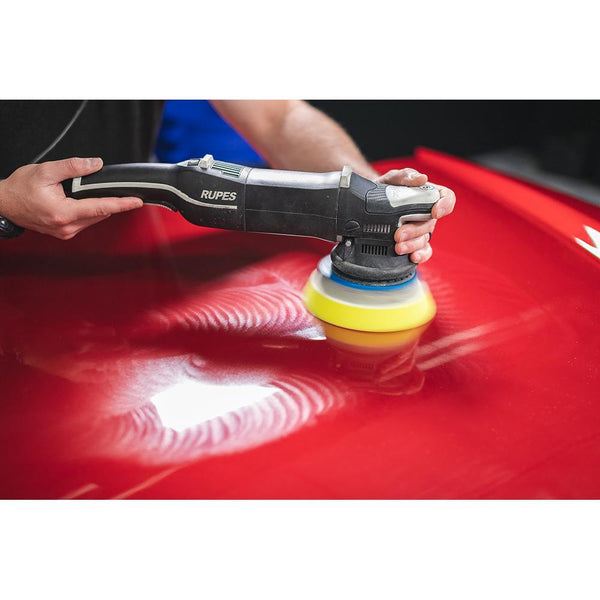 A closeup of a person using a polisher on the hood of a red car.