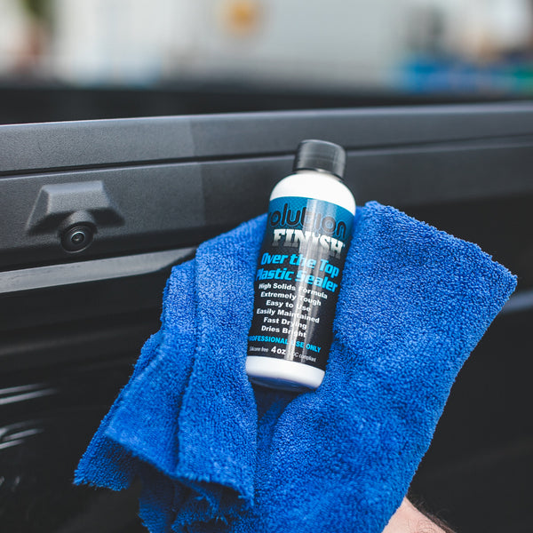A bottle of Solution Finish Over the Top Plastic Sealer on a blue towel on a car dashboard.