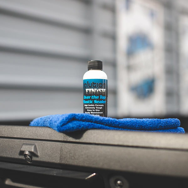 A bottle of Solution Finish Over the Top Plastic Sealer on a blue towel on a car dashboard.
