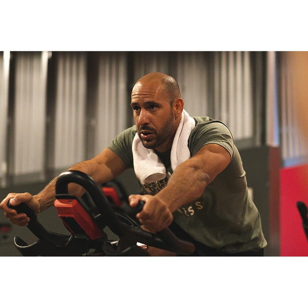 A person on a peloton with a white Spa and Workout towel wrapped around their neck.