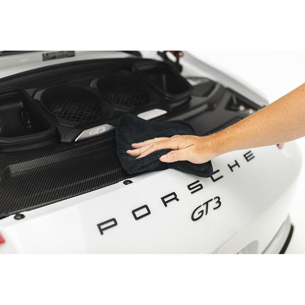 A closeup of a hand holding a black spectrum 420 towel using it to clean the back of a Porsche.