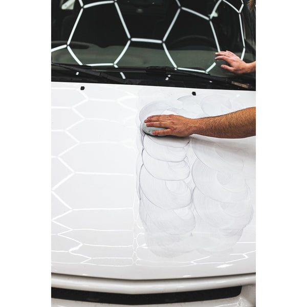 A closeup of a person scrubbing the hood of a white car.