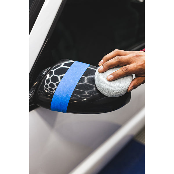 A person scrubbing a white car's side mirror with a grey applicator.
