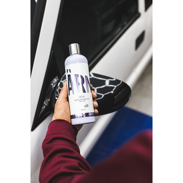 A closeup of a person holding a bottle of Stjarnagloss Skara in front of a white car.