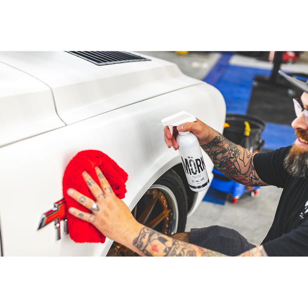 A closeup of a person spraying Stjarnagloss Matt Finish Detailer on a white car and wiping it with a red rag.