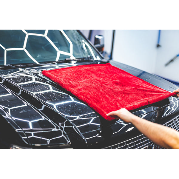 A person spread a red 1500 towel across a black car hood.