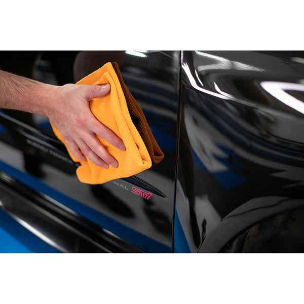 Using an orange Edgeless Pearl microfiber towel from The Rag Company to detail the door of a black 2004 Subaru WRX STI