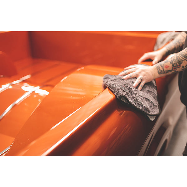 A closeup of a person wiping an orange truck with a grey Gauntlet towel.