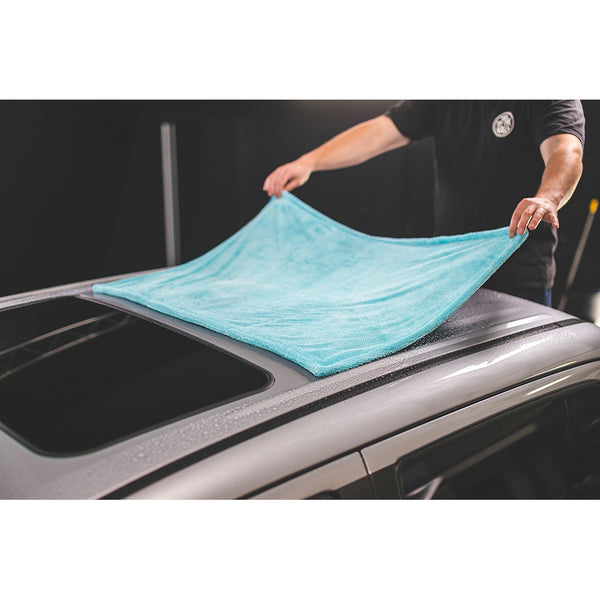 A person spreading a liquid8r towel across the roof of a car.