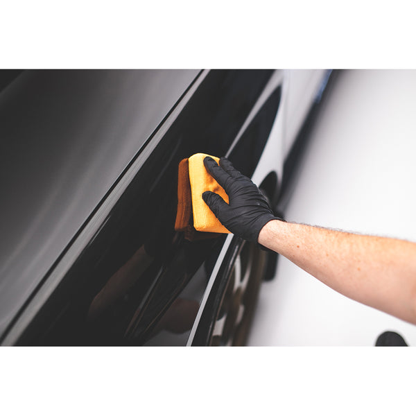 A closeup of a person wiping a black car with an orange pearl sponge.