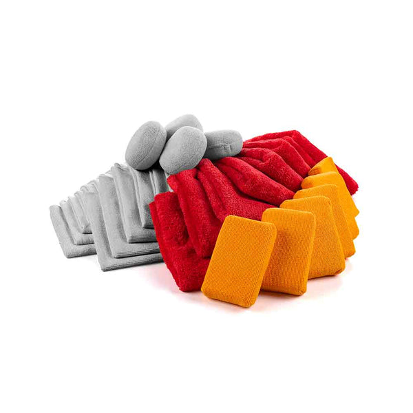 A collection of microfiber car detailing pads and towels in three different colors: gray, red, and yellow. The set includes rectangular pads, circular applicator pads, and folded towels. Each color group is neatly arranged, showcasing the variety of products available for different detailing needs.