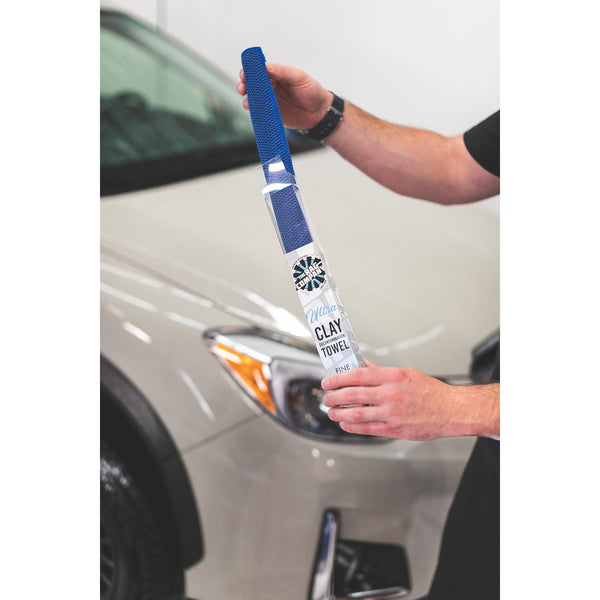 A closeup of someone taking an Ultra Clay towel out of its packaging with a background of a beige car.