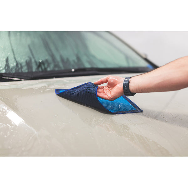 A closeup of someone folding over a blue wet Ultra Clay towel on the hood of a beige car.
