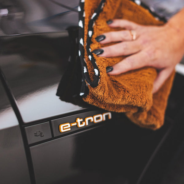 A person scrubbing a black car with a brown Wolfpack towel.