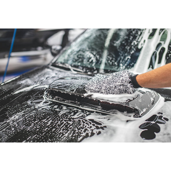 A closeup of someone using The Rag Company Ultra Wash Mitt on the hood of a black car covered in foam.