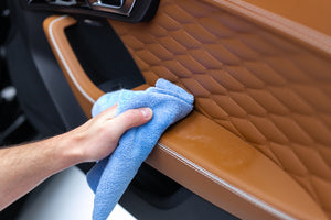 Person cleaning a car's brown car door interior with a blue edgeless 300 rag.