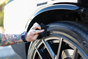 A person cleaning a tire eith a black applicator sponge.