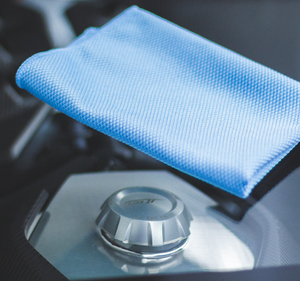 Close-up of a light blue diamond microfiber cloth resting on a metallic surface near a fuel cap labeled 'GT1'.