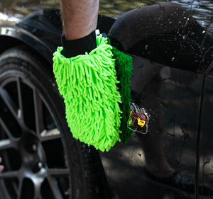 A person drying off a black truck with a green Chenille Knobby Mitt.