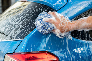 A person scrubbing a blue car's taillight with a Cyclone Bone Sponge.