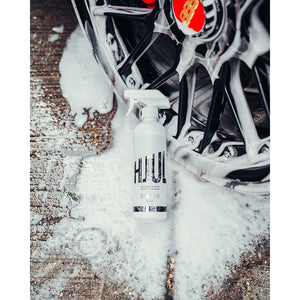 A wheel rim covered in suds laying on the sudsy ground with a spray bottle of Stjarnagloss Colour Change Wheel Cleaner resting on it.