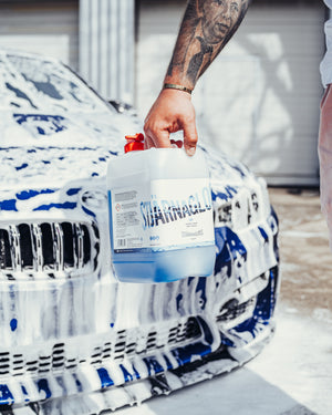 a person holding the Stjarnagloss Sno in front of a blue car covered in foam.