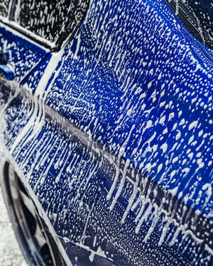 The side of a blue car covered in cleaning foam.