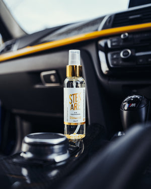 A bottle of Stekare Gold Air Freshener on the center console of a car.