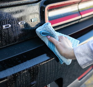 Using a light blue Dry Me A River microfiber towel from The Rag Company to dry the bumper of a black Dodge Challenger