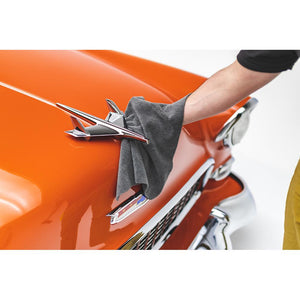 A person drying a hood ornament of an orange classic car with a grey edgeless towel.