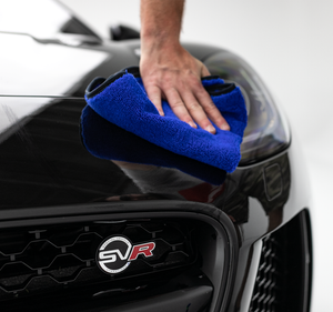 A person drying off the front of a black car with a dark blue Spectrum 420 towel.