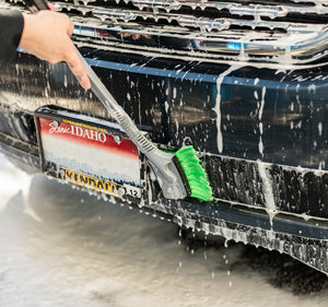 A person cleaning the front of a foamy car with a long Wheel and Body rush.