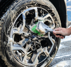 A person scrubbing a foamy car tire with A Wheel and Body Brush.