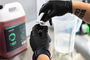 Person wearing black gloves holding a spray bottle with Armour Detail Clean inside of it.