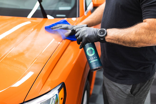 A person spraying Armour Detail Panel on an orange car and wiping it with a blue towel.