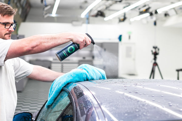 A person spraying the roof of a car with Armour Ceramic Spray Sealant and wiping it with a blue towel.