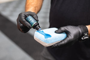 A closeup of a person pouring Armour Quartz Coating on a blue applicator sponge.