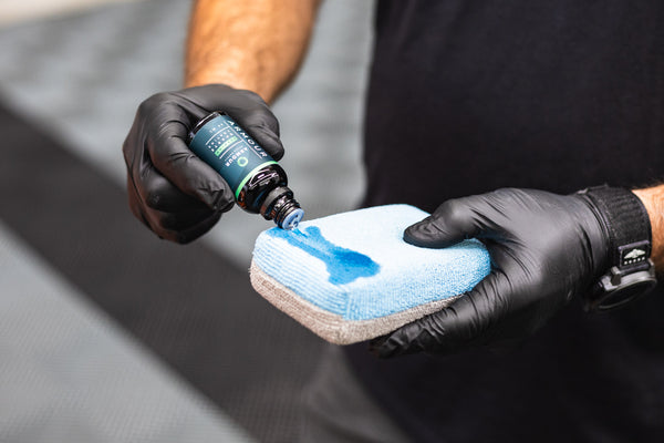 A closeup of a person pouring Armour Detail Quartz Coating onto a blue and grey applicator sponge.