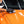 A closeup of a person cleaning the hood of an orange car with a blue and grey applicator sponge.