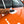 A closeup of a person cleaning the hood of an orange car with a while paper towel.