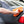 A closeup of a person scrubbing the back of a grey car with an orange towel.