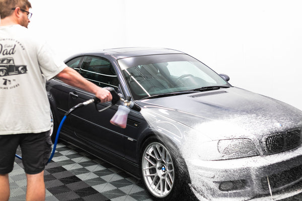 A person foaming a grey car in a studio with a foam cannon. 