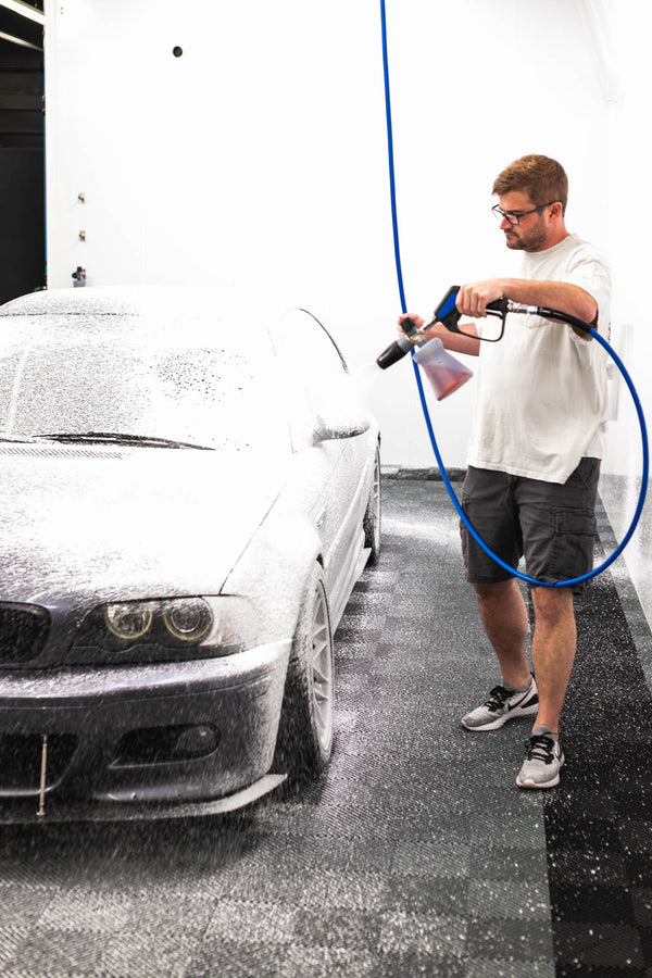 A person foaming a grey car in a studio with a foam cannon. 